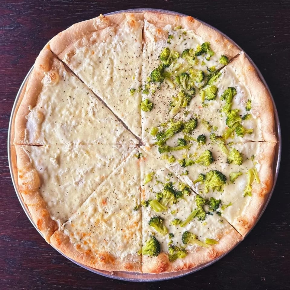 Round cheese pizza topped with broccoli florets, sliced into eight pieces on a metal tray over a dark wooden table.