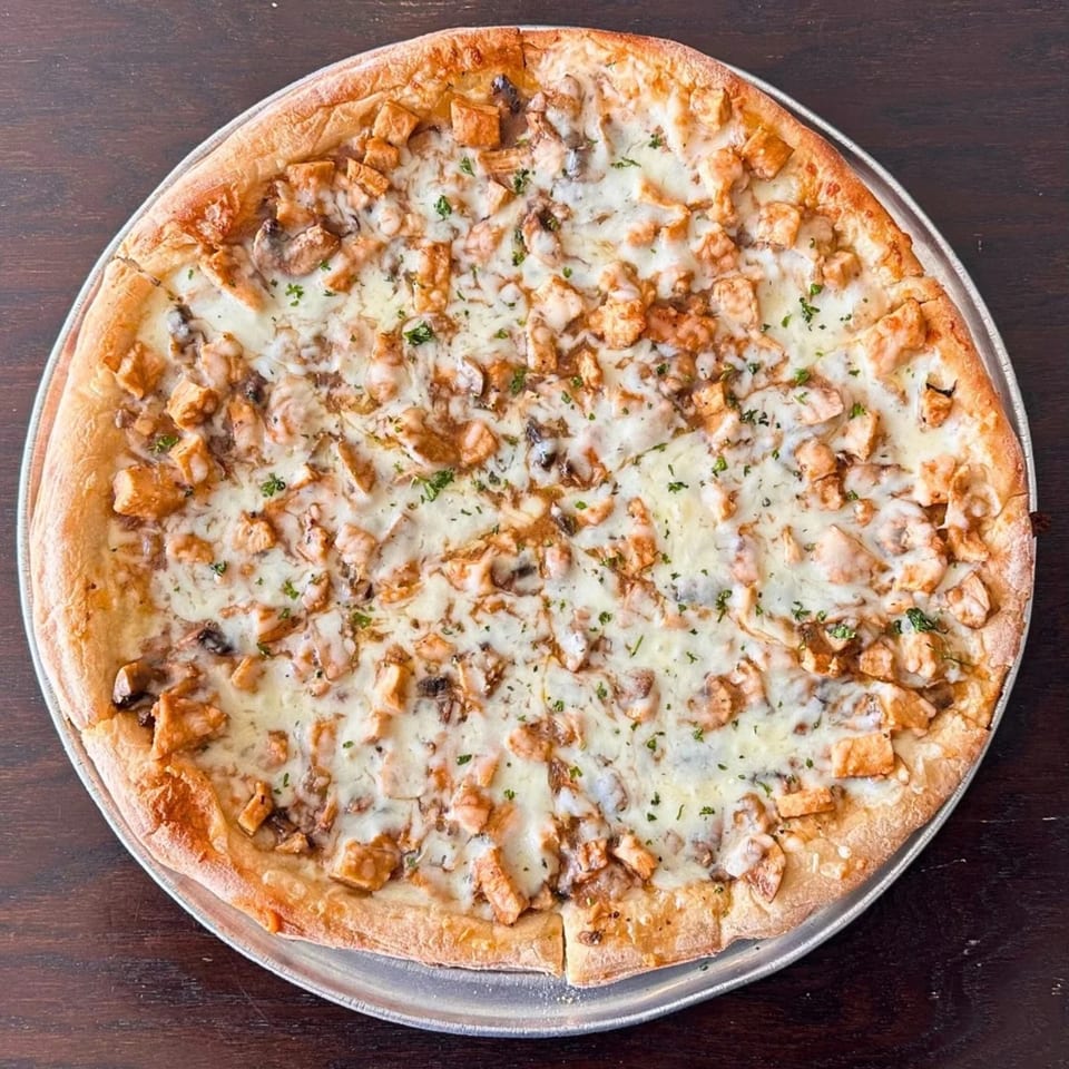 Large thin-crust pizza topped with melted cheese, diced chicken, mushrooms, and herbs on a metal tray.