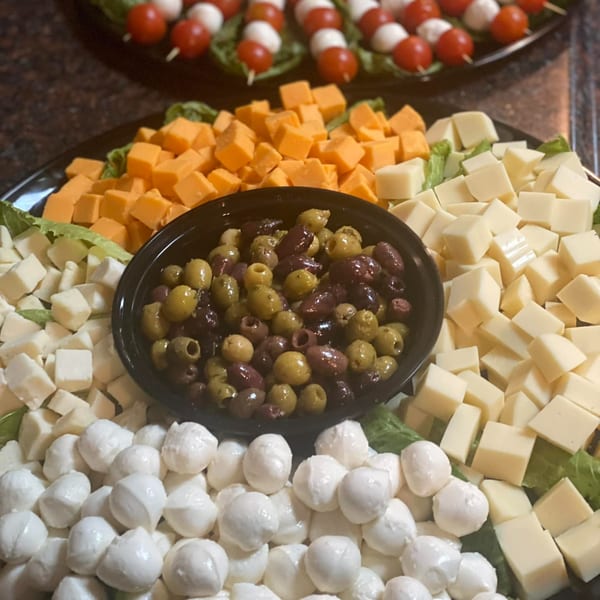 A platter of cubed cheeses, mozzarella balls, and olives, with tomato and mozzarella skewers in the background.