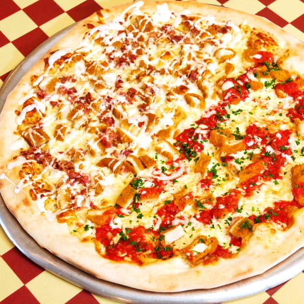 Half white pizza with chicken and bacon, half red pizza with chicken and parsley on a checkered tablecloth.