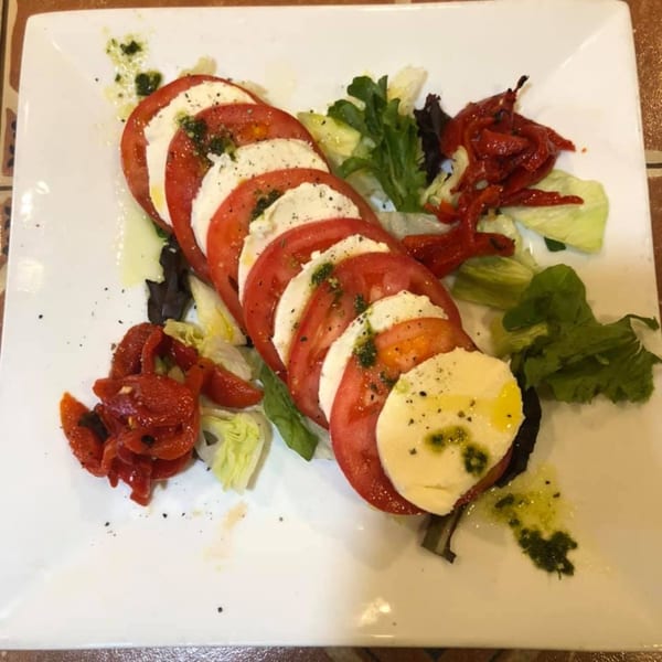 Caprese salad with sliced tomatoes, mozzarella, pesto, and roasted red peppers on a white plate.