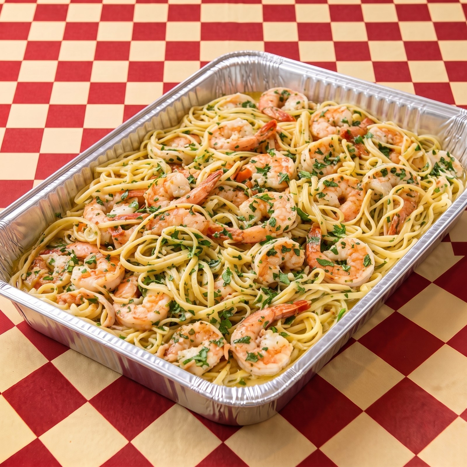 Aluminum catering tray filled with shrimp linguine garnished with parsley on a red-and-cream checkered tablecloth.